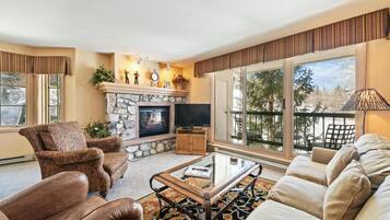 A living room with a fireplace, leather armchairs, a sofa, a glass coffee table, and a large window with a view.