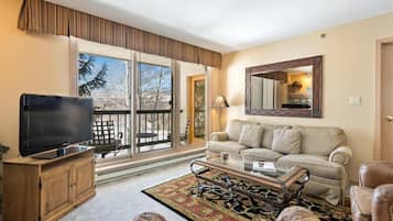 A living room with a television, sofa, coffee table, and a large window.