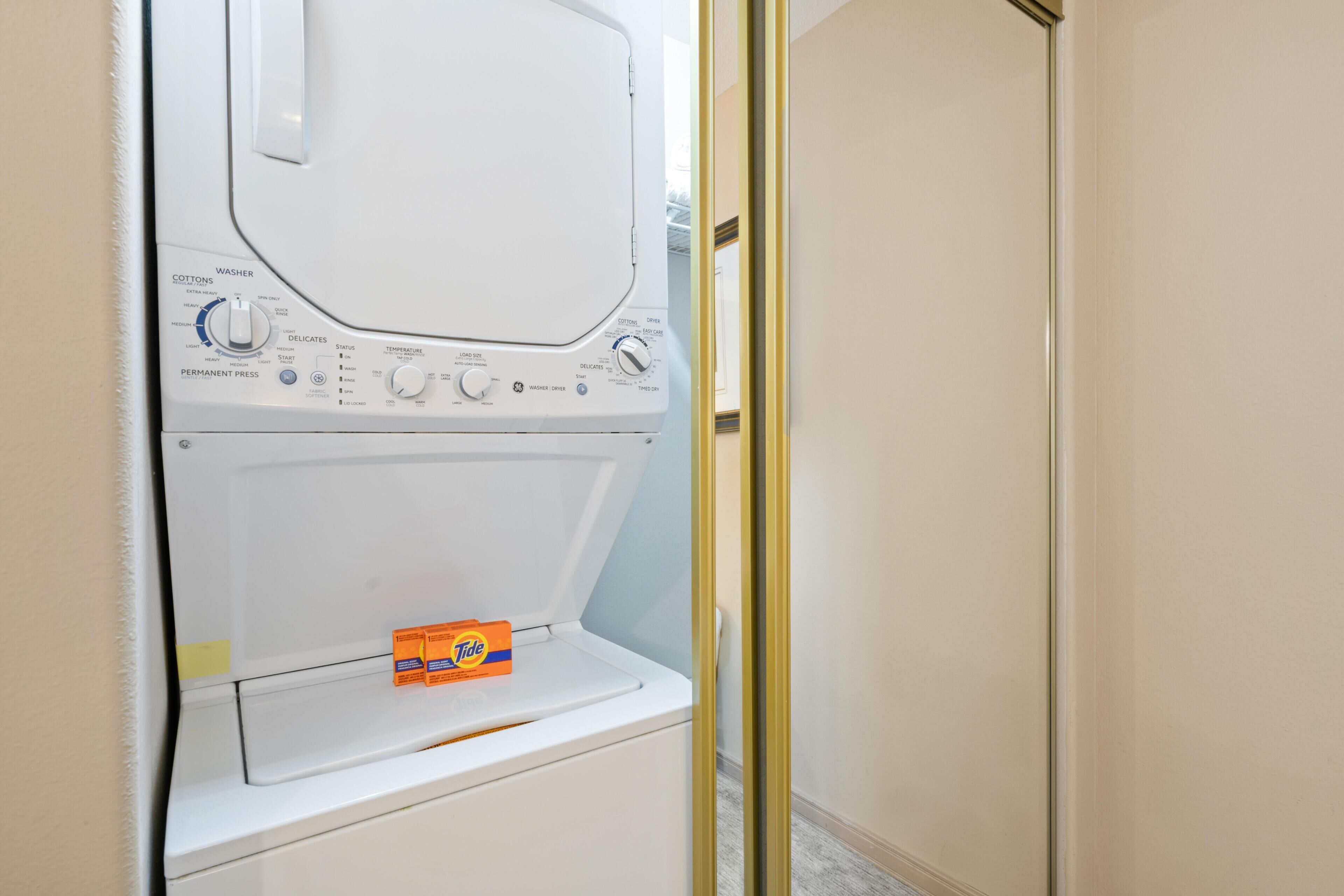A front-loading washing machine with a Tide detergent box on the door.