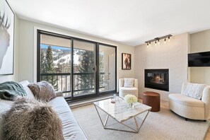 A modern living room with a large window, a fireplace, and a cozy seating area. - Borders Lodge L402 2BD Beaver Creek Ski-in, Ski-out Condo (Avon)