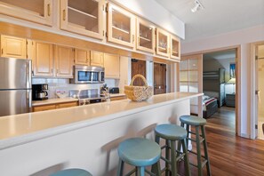 A kitchen with wooden cabinets, a microwave, a refrigerator, and a bar area with stools. - Borders Lodge L403 2BD Beaver Creek Ski-in, Ski-out Condo (Avon)