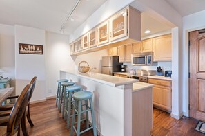 A kitchen with wooden cabinets, a central island with stools, a refrigerator, and a microwave. - Borders Lodge L403 2BD Beaver Creek Ski-in, Ski-out Condo (Avon)