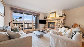 A living room with a stone fireplace, a large window, and a balcony.