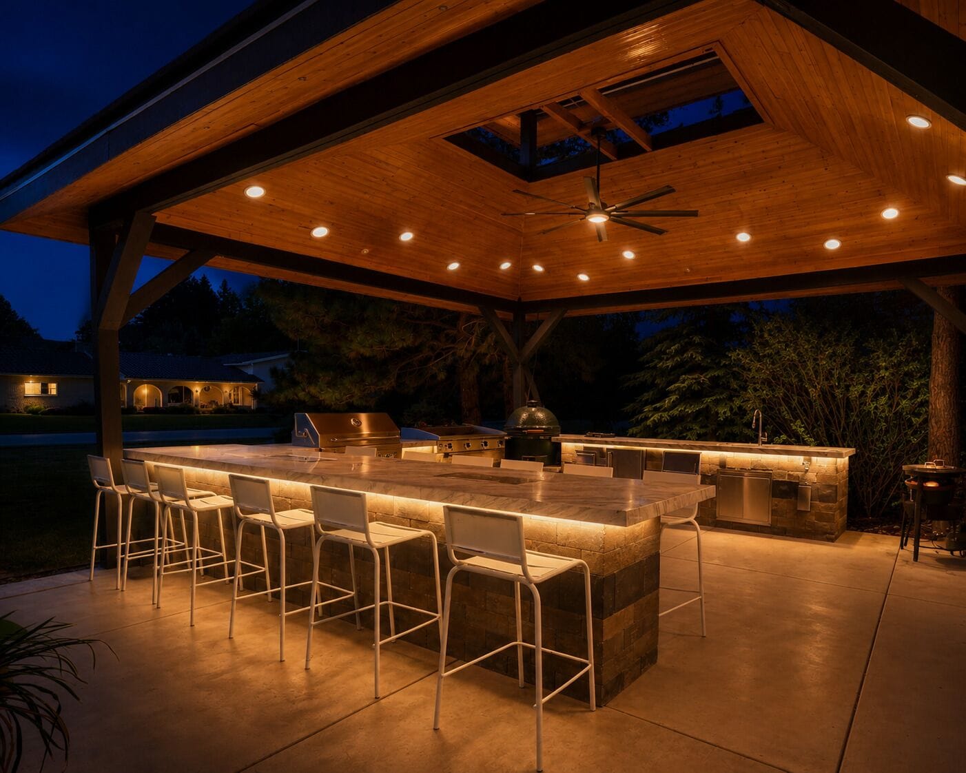 An outdoor kitchen area with a bar and seating, under a wooden pergola with a ceiling fan.