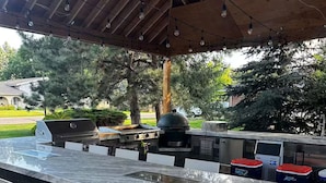 Ett utomhuskök med en grill, barstolar och en pergola som tak.
