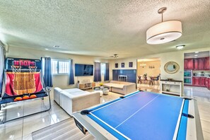 Ein Wohnzimmer mit Billardtisch, Basketballkorb, Sofa und Fernseher.