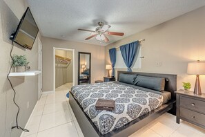 Ein Schlafzimmer mit Bett, Nachttischen, Deckenventilator, Fernseher und einem Badezimmer mit Spiegel und Handtuchhalter.