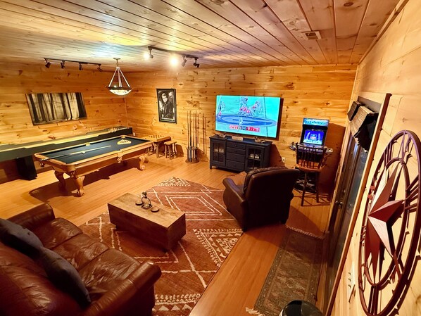 Ein Holzinnenraum mit Pooltisch, Ledersofa und einem Fernseher, der ein Spiel zeigt.