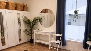 Een kamer met houten vloer, witte kasten, een bureau, een spiegel en een raam met gordijnen.