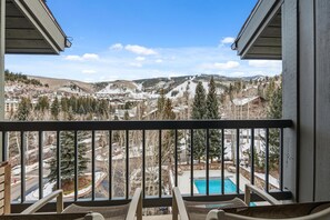 Un balcon offrant une vue sur un paysage montagneux enneigé, une piscine et un ciel dégagé.