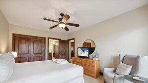 Un dormitorio con cama, cómoda, televisor, silla y ventilador de techo.