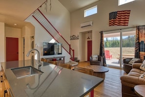 Una cocina moderna con una isla grande, un comedor con una silla roja, un sofá y vistas al exterior.