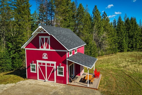 A red barn with a porch and a table, surrounded by a forest.