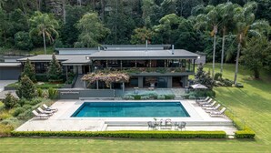 Et moderne hus i to etager med swimmingpool, udendørs møbler og frodig beplantning.