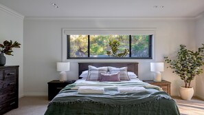 A bedroom with a large window, a bed with a green bedspread, two bedside tables with lamps, and a dresser. - Grants Retreat - spacious riverside escape on the Shoalhaven River (Longreach)