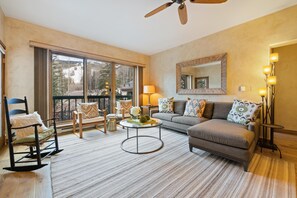 Ein geräumiges Wohnzimmer mit großem Fenster, Deckenventilator, Sofa, Couchtisch und Sessel.