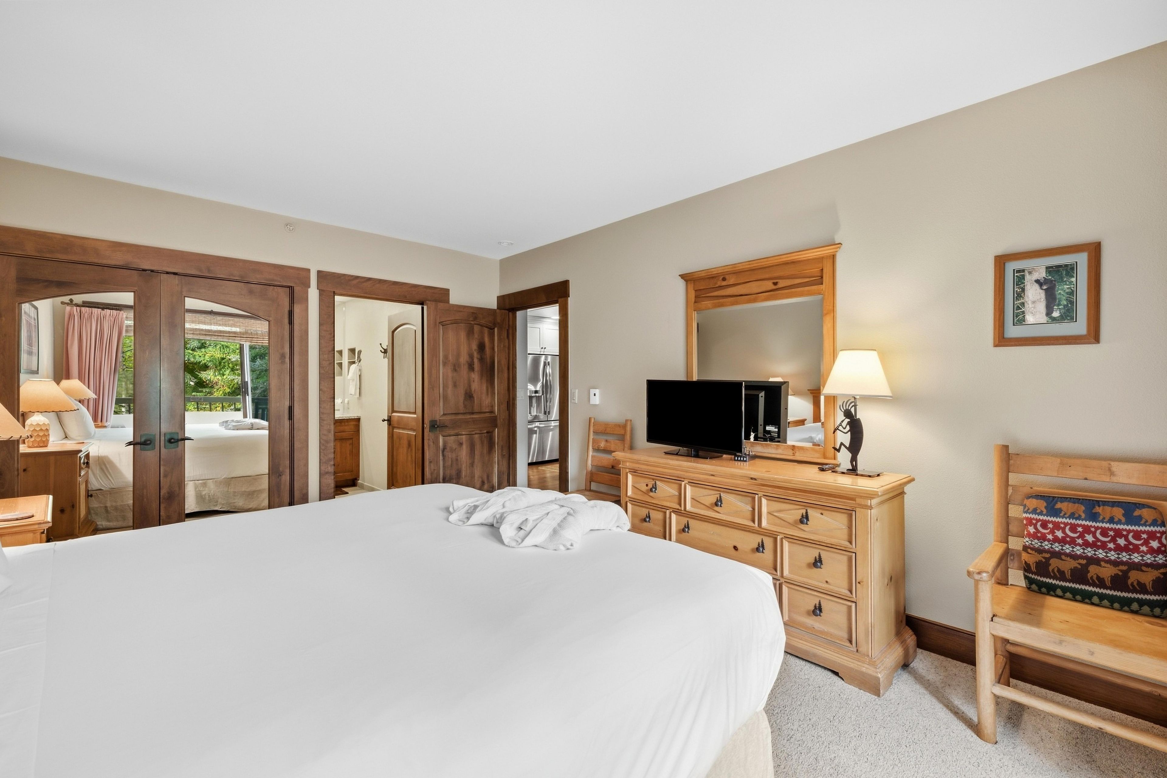 A bedroom with a large bed, wooden wardrobe, a television, and a chair.