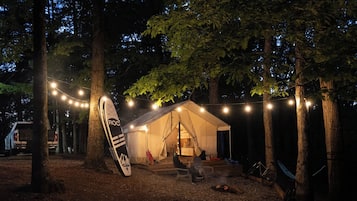A tent with a sleeping area and a chair, surrounded by trees and string lights.