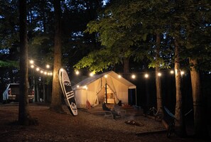 A tent with a sleeping area and a chair, surrounded by trees and string lights.