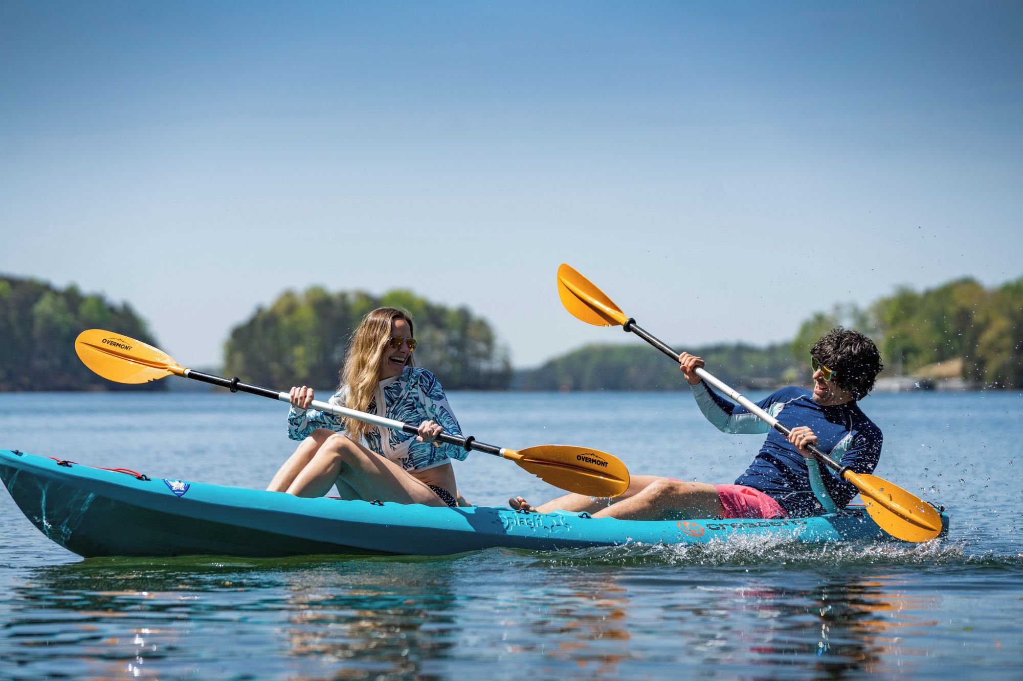 Deux personnes pratiquent le kayak sur un lac paisible, sous un ciel dégagé.