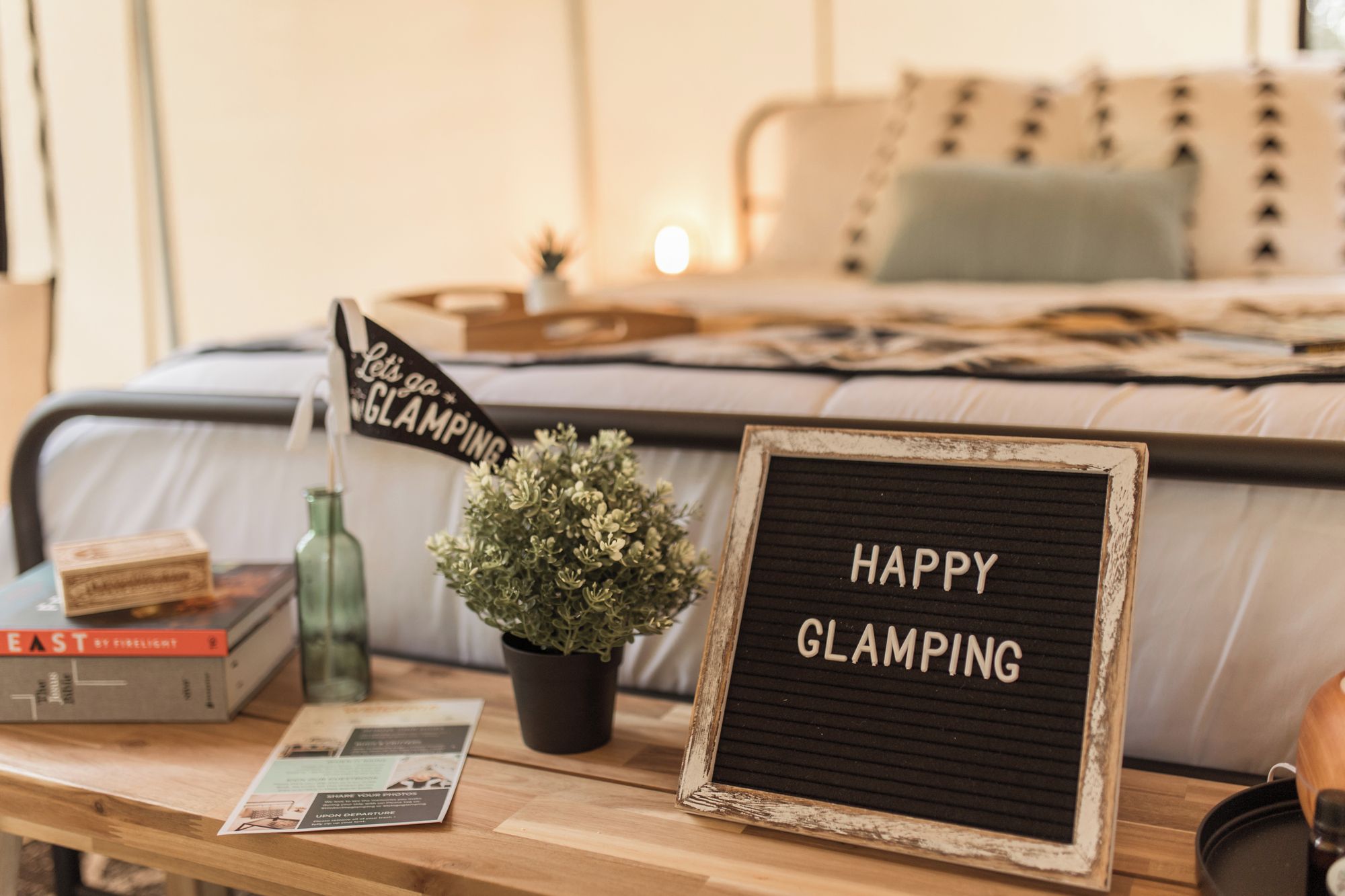 En seng med et skilt, der står 'HAPPY GLAMPING', og en lille urtepotte på en sengebord.