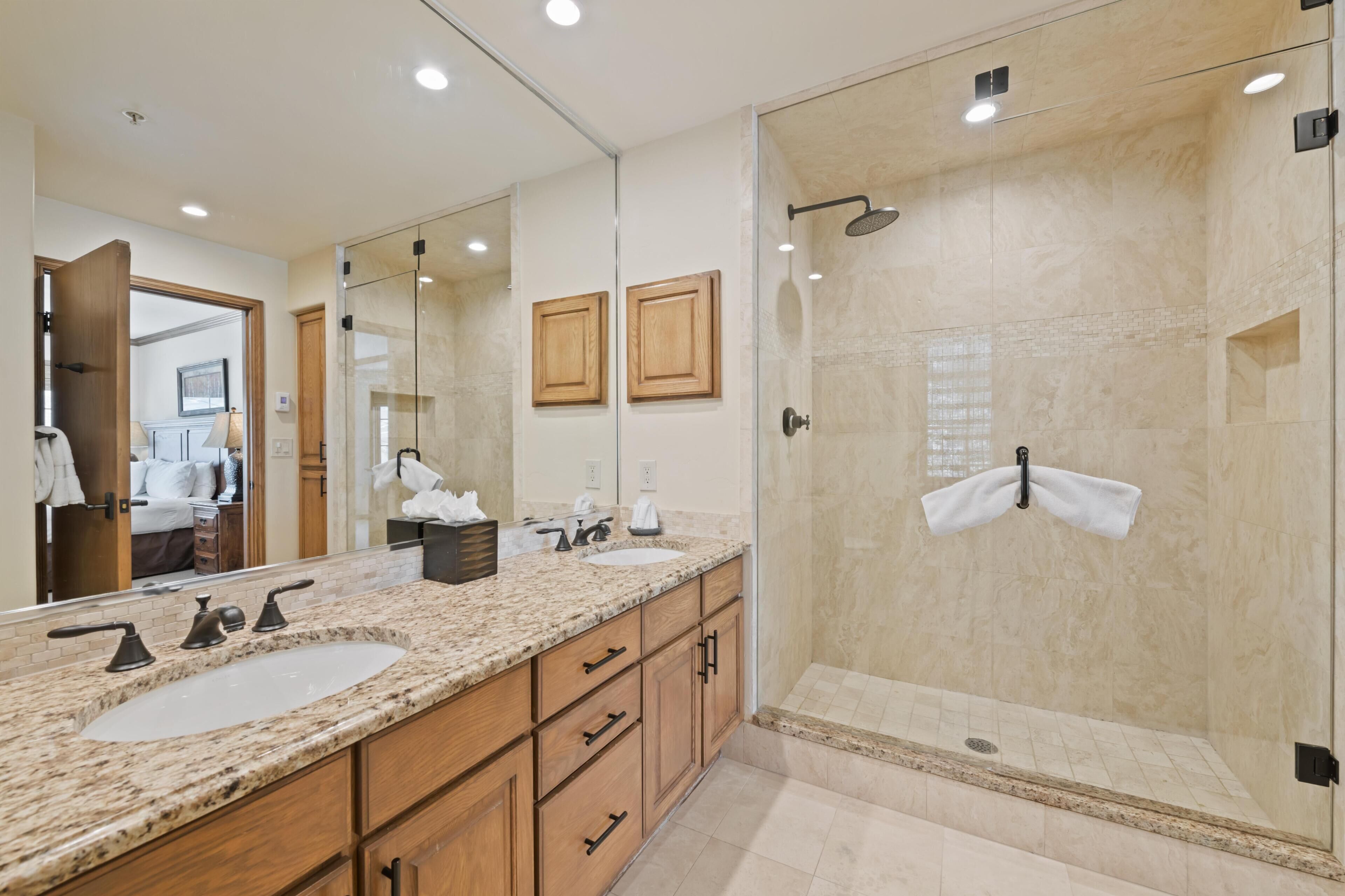 Une salle de bain avec un comptoir en granit, un lavabo, un miroir, des armoires en bois, une douche en verre et une serviette accrochée au mur.