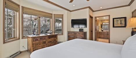 A bedroom with a large bed, wooden dresser, TV, and a ceiling fan.