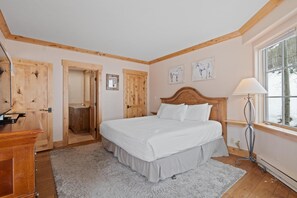 A bedroom with a wooden headboard, a bed with white bedding, a bedside lamp, a window with a view, and a door leading to a bathroom. - Borders Lodge U301 2BD Beaver Creek Ski-in, Ski-out Condo (Avon)
