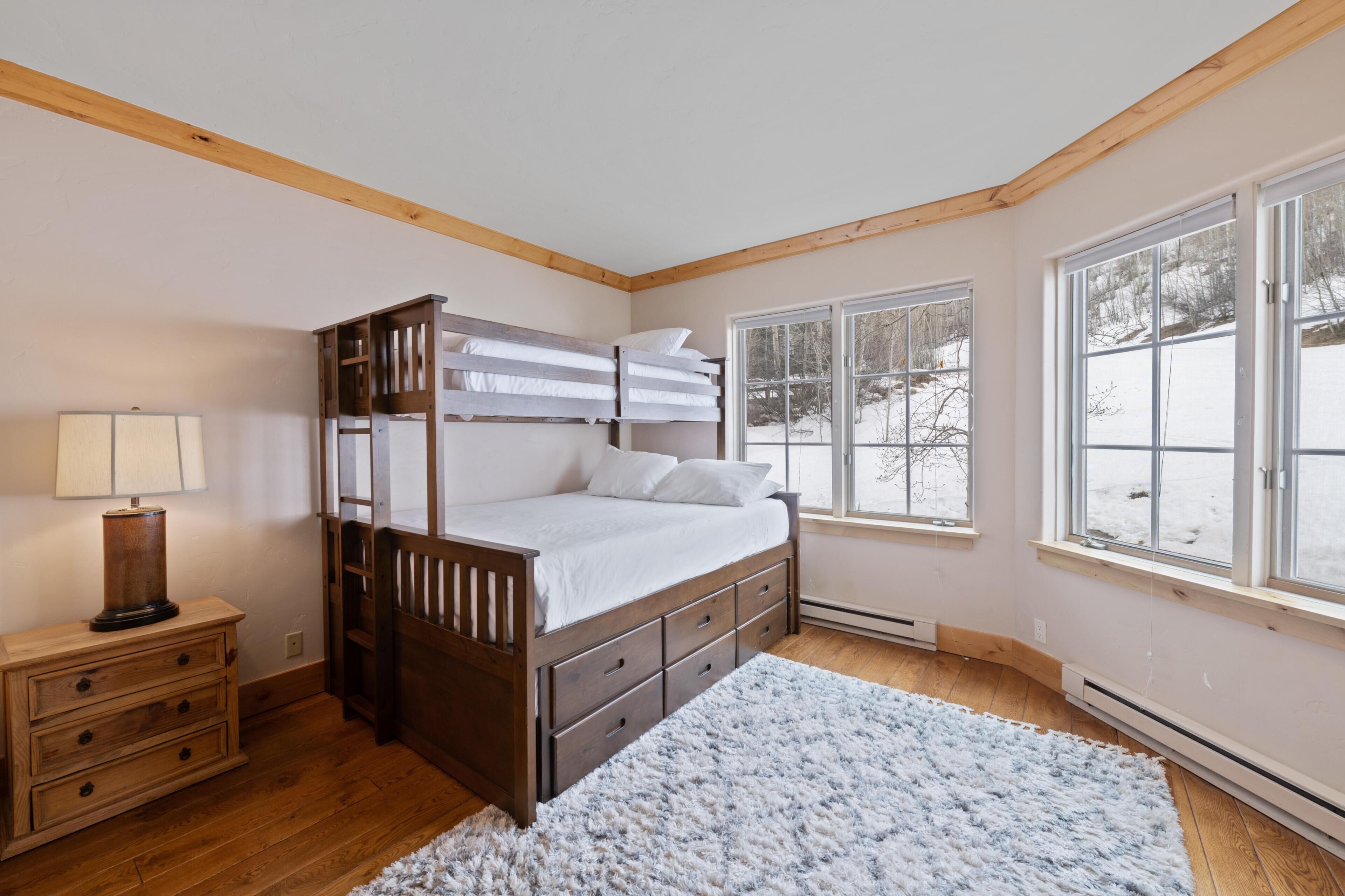 A bedroom with a wooden bed, a nightstand, a lamp, a window with a view of a snowy landscape, and a white rug.