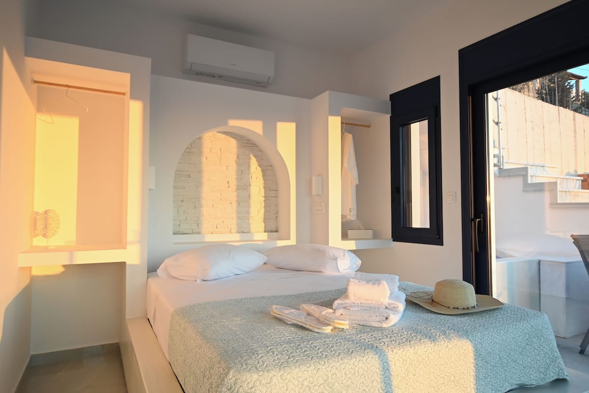 A bedroom with a bed, a towel, a hat, and a window.