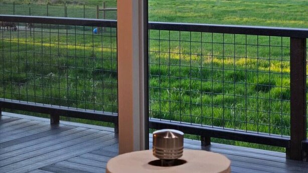 A balcony with a view of a green field and forested hills.
