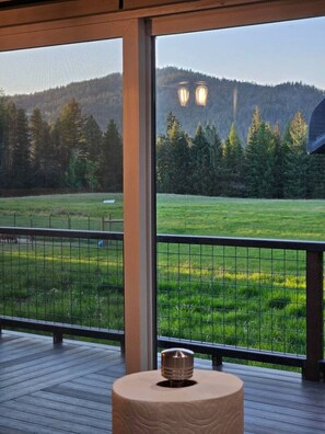 Un balcon donnant sur un champ verdoyant et des collines boisées.