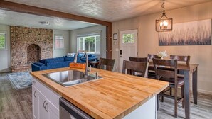 A kitchen with a wooden countertop, a sink, and a dining area with chairs and a table.