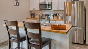 A kitchen with white cabinets, a stainless steel refrigerator, a microwave, and a sink.