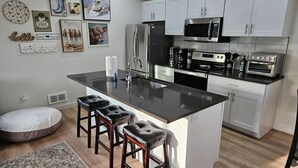 Una cocina moderna con una isla central, taburetes de bar, gabinetes blancos, electrodomésticos de acero inoxidable y obras de arte en las paredes.