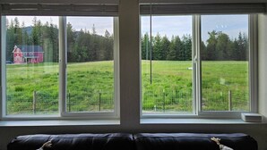 Una habitación con dos ventanas amplias que dan a un campo verde y un granero rojo.