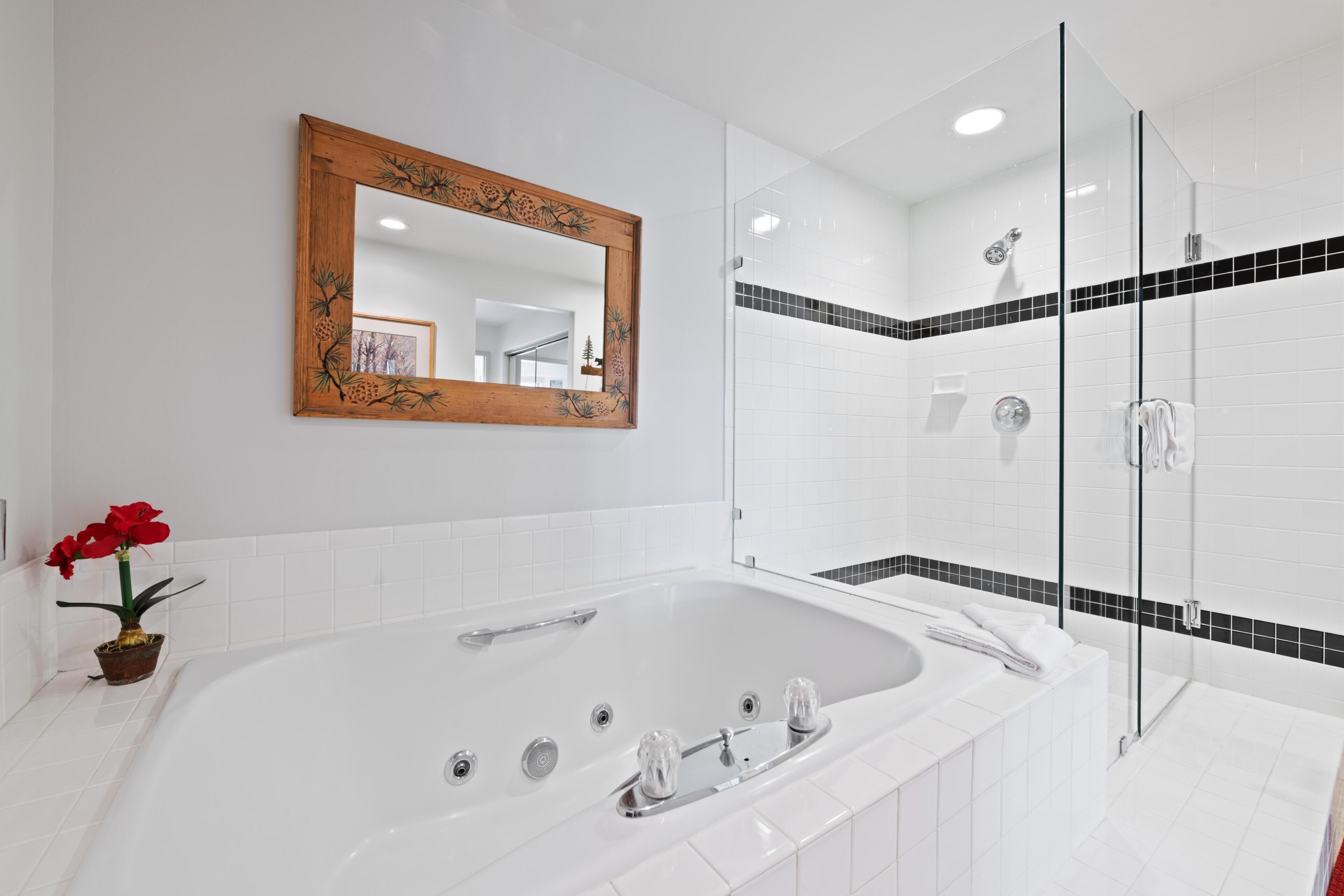 A modern bathroom with a large bathtub, a glass-enclosed shower, and a wooden-framed mirror.
