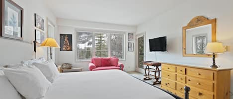 Un dormitorio con una cama grande, un aparador, un televisor y una ventana que da a vistas de árboles.