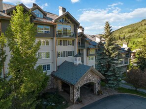 Un hotel de varios pisos con entrada de piedra, balcones y vistas del paisaje circundante.
