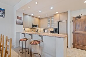 Una cocina moderna con una isla central, taburetes de bar, electrodomésticos de acero inoxidable e iluminación empotrada en el techo.