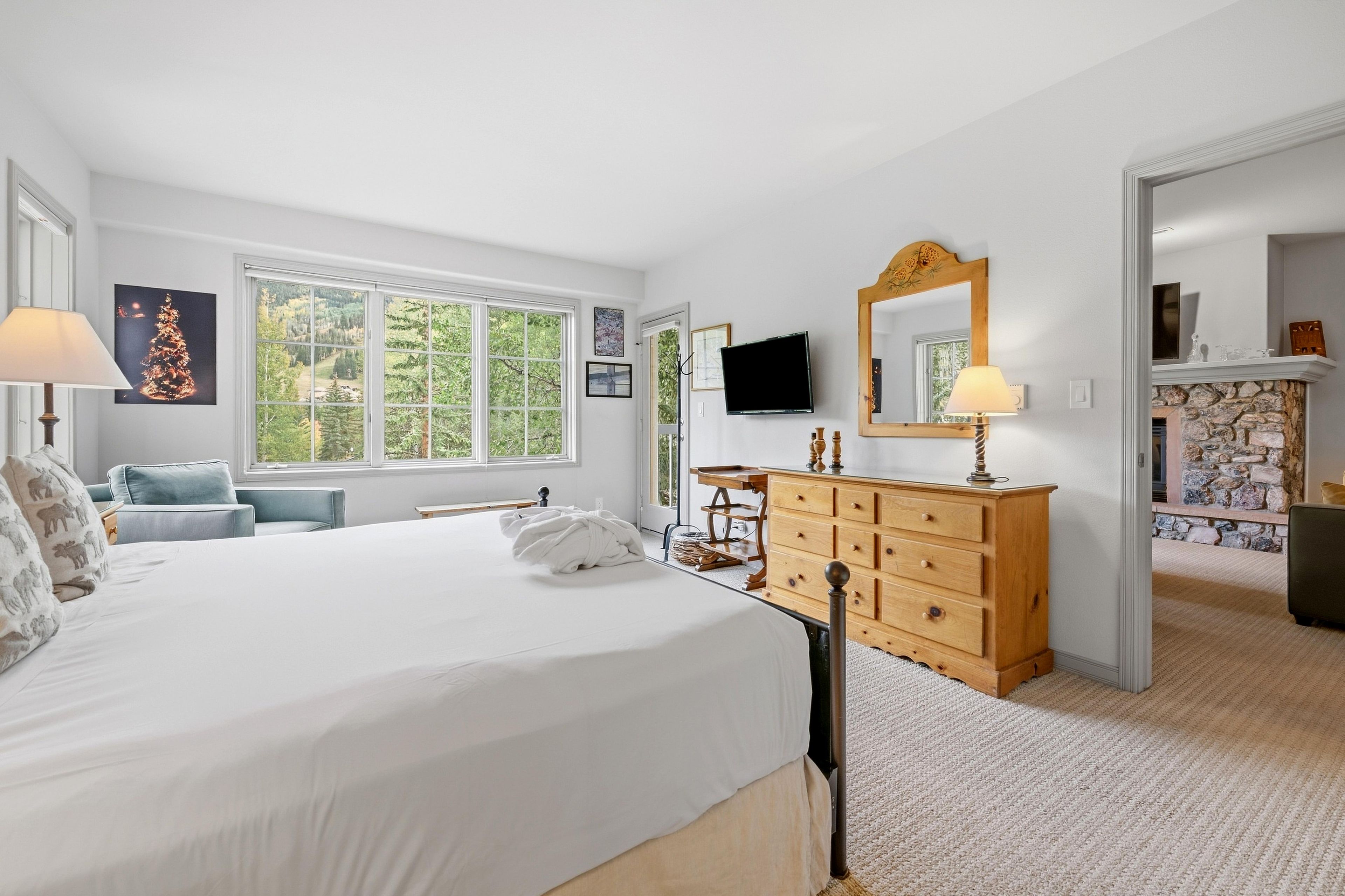 A bedroom with a large bed, a dresser, a television, and a stone fireplace.