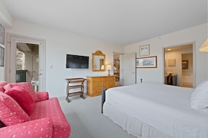 Un dormitorio con cama, cómoda, televisor, espejo y sofá rojo.
