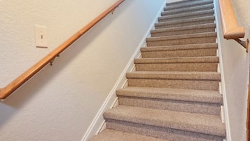 A carpeted staircase with wooden handrails, white walls, and a light switch.