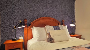 A bed with a wooden headboard, two bedside tables with lamps, a clock, and a patterned quilt.