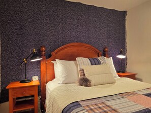Ein Bett mit hölzernem Kopfteil, zwei Nachttische mit Lampen, einer Uhr und einer gemusterten Bettdecke.