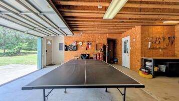 A ping pong table in a garage with wooden walls, a door, and various tools on the wall.
