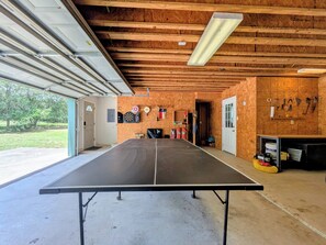 Ein Pingpongtisch in einer Garage mit Holzwänden, einer Tür und verschiedenen Werkzeugen an der Wand.