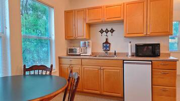 A kitchen with wooden cabinets, a dishwasher, a microwave, a coffee maker, and a dining table with chairs.