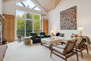 Ein geräumiges Wohnzimmer mit großem Fenster, Holzmöbeln und einem modernen abstrakten Gemälde.