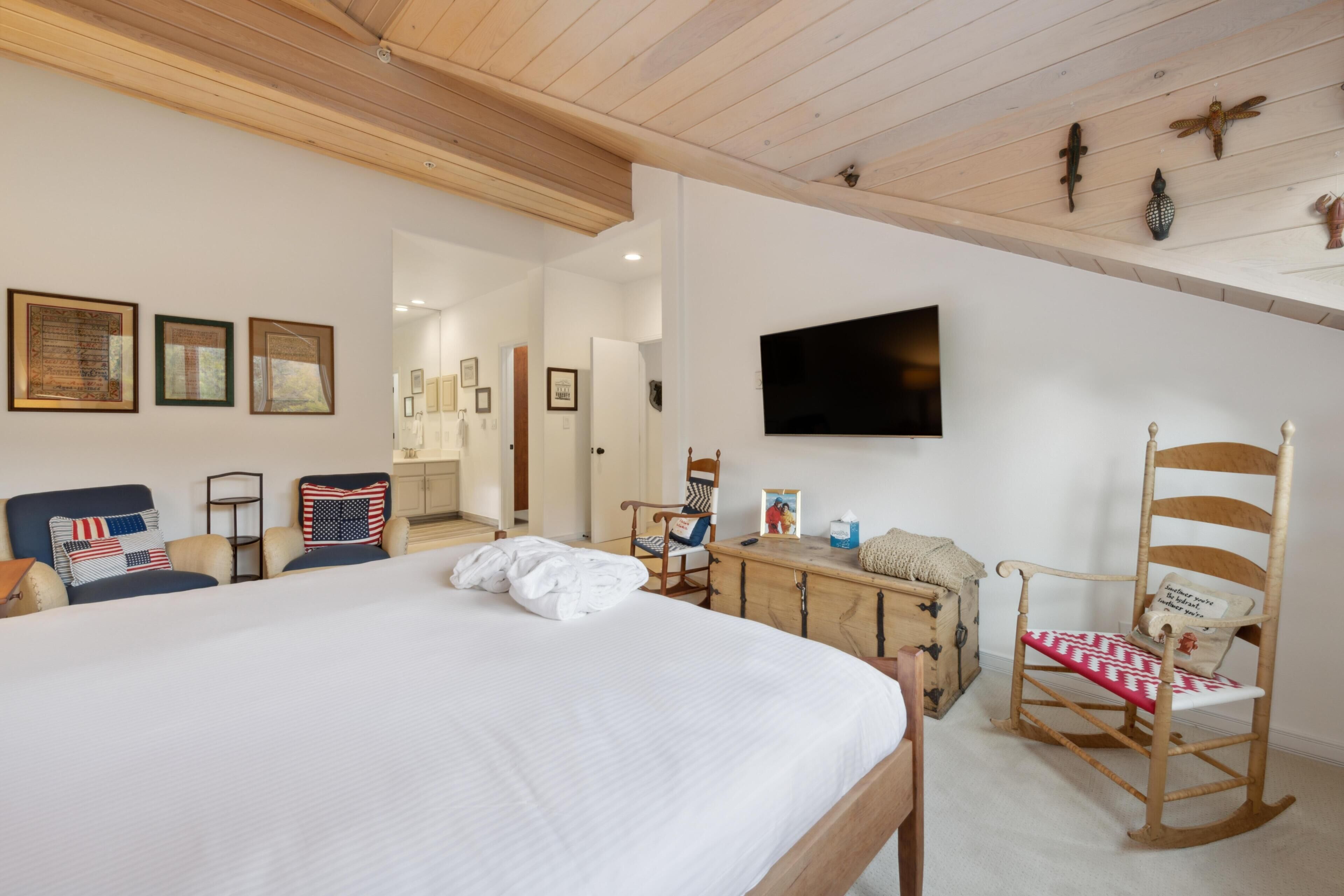Een slaapkamer met een groot bed, een houten schommelstoel, een televisie en decoraties aan de muur.
